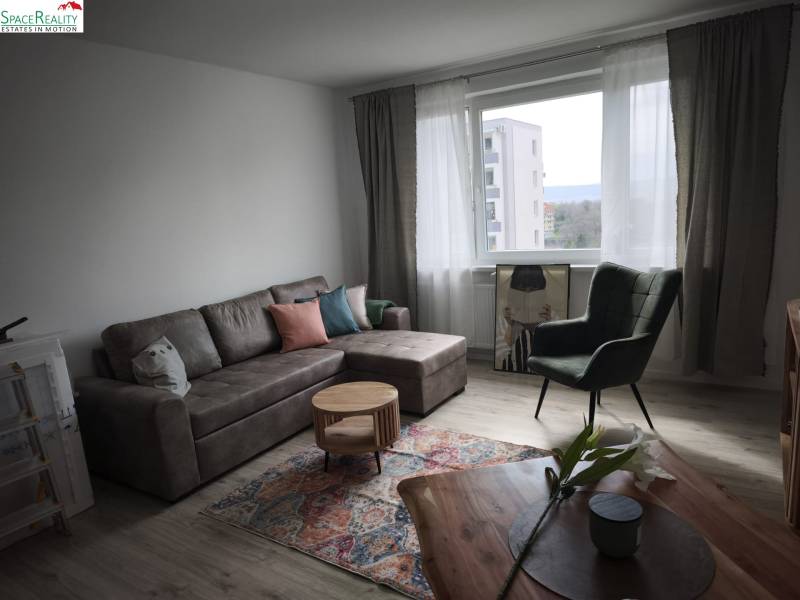 Obývacia izba v 2-izbovom byte s podlahou s dreveným dekorom a pohodlnou sedacou súpravou.