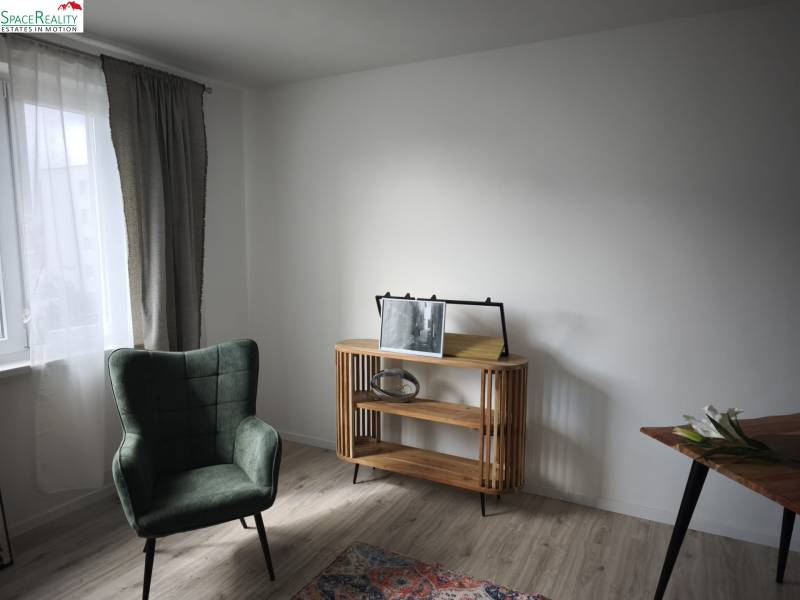 Izba v 2-izbovom byte s kreslom, stolíkom a podlahou s dreveným dekorom.