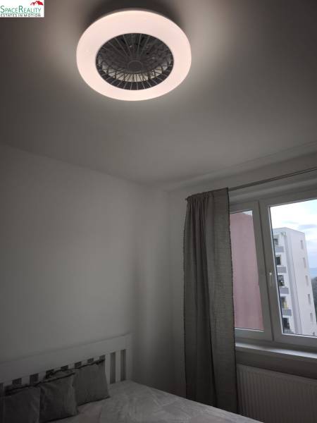 Spálňa v 2-izbovom byte so stropným ventilátorom a oknom s výhľadom.
